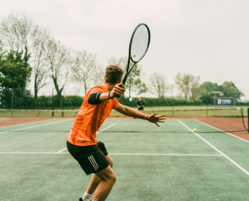 man in orange shirt and black shorts holding black and white tennis racket