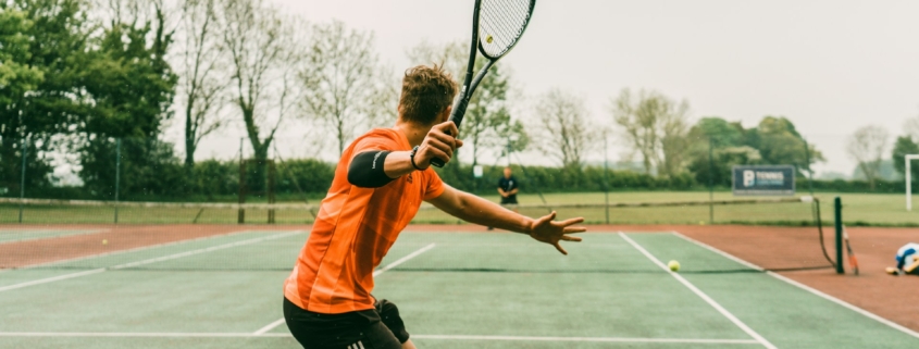 man in orange shirt and black shorts holding black and white tennis racket