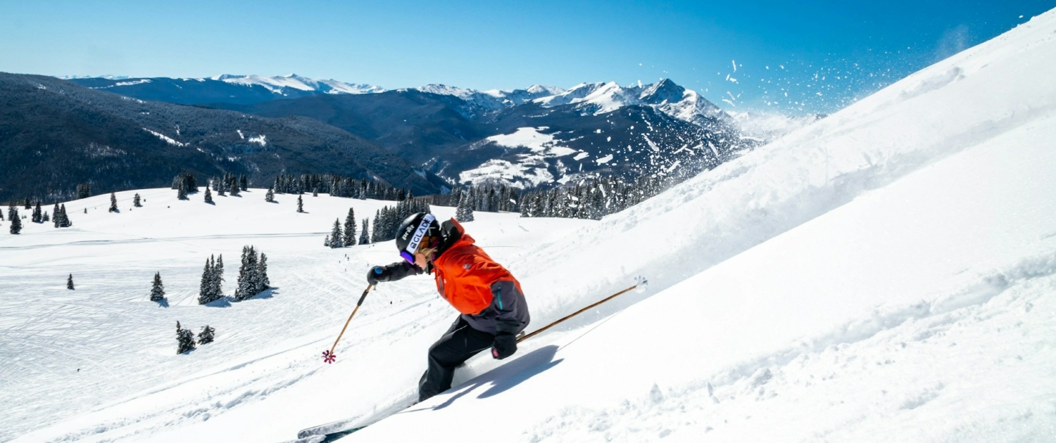 person in orange jacket and black pants riding ski blades on snow covered mountain during daytime