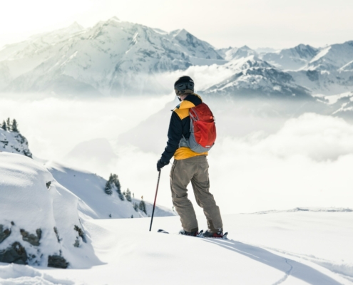 man in orange jacket and brown pants standing on snow covered mountain during daytime