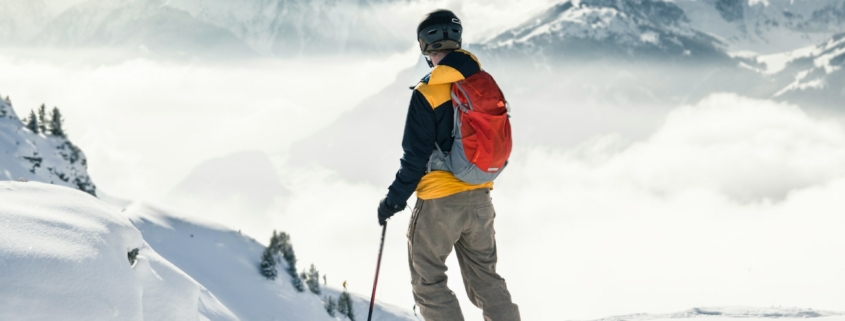 man in orange jacket and brown pants standing on snow covered mountain during daytime