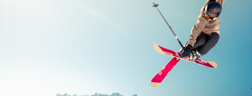 person in brown jacket doing snow ski blade trick